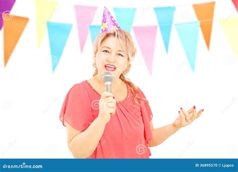 Mature Lady With Party Hat Singing On Microphone At A Birthday P Stock