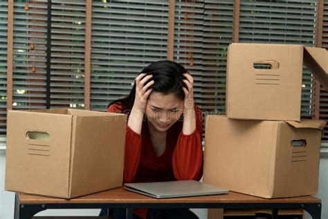 sad asian woman packing belongings in a cardboard box and crying on the desk in the office after