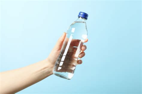 Premium Photo Female Hand Holds Bottle With Water On Blue Close Up