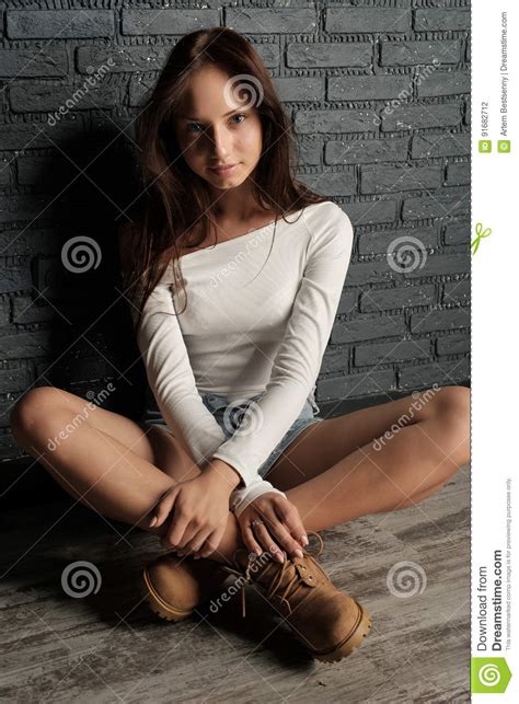 Jeune Brune Dans La Chemise Blanche Les Shorts Et Les Bottes Se Reposant Sur Le Plancher En