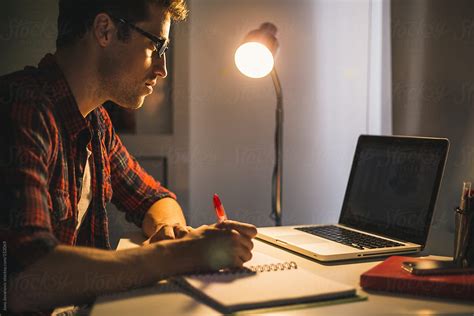Young Man Working Late At Home Sitting At His Desk By Stocksy