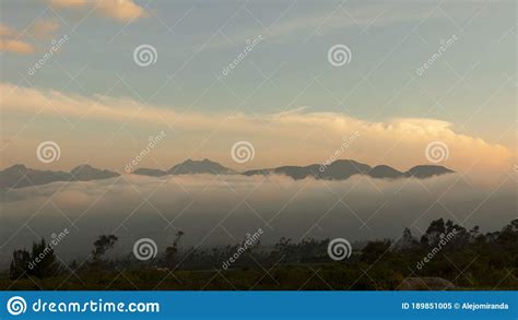 Green Field With Dense Layer Of Clouds With Mountains In The Background