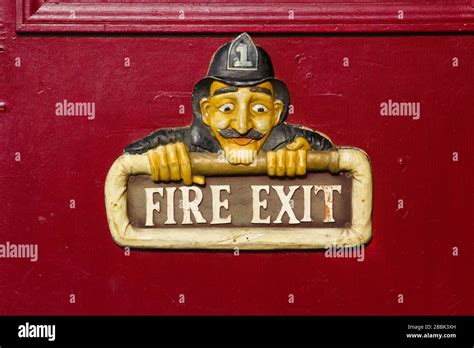 A Wooden Fire Exit Sign With A Cartoon Fireman Hanging On A Red Door