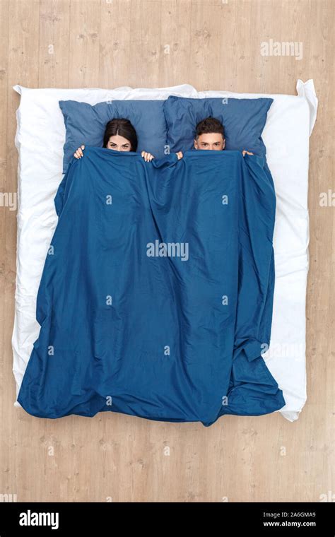 Bedtime Young Couple Lying On Bed Hiding Under Blanket Top View Looking Camera Playful Stock