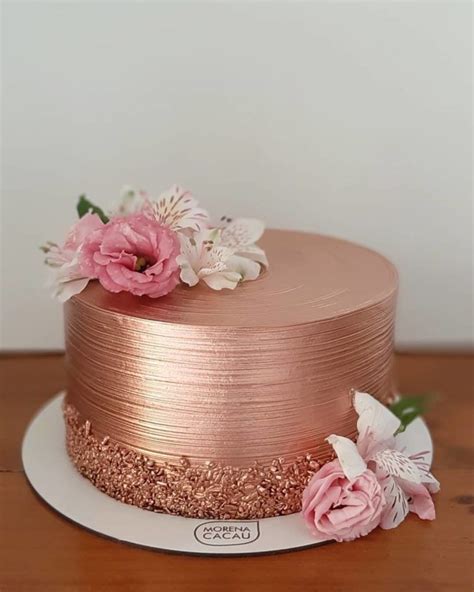 There Is A Pink Cake With Flowers On The Top And Gold Frosting Around It