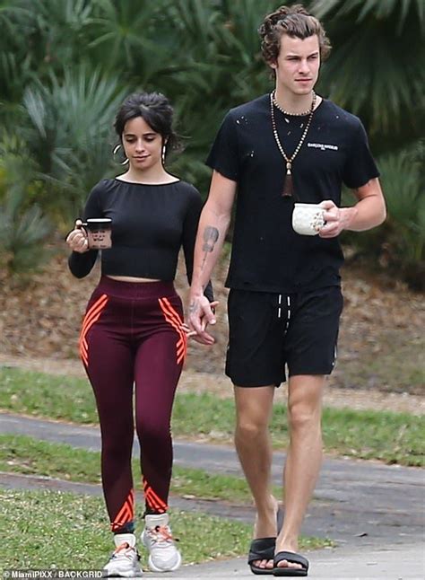 The Man And Woman Are Walking Down The Street Holding Coffee Cups In