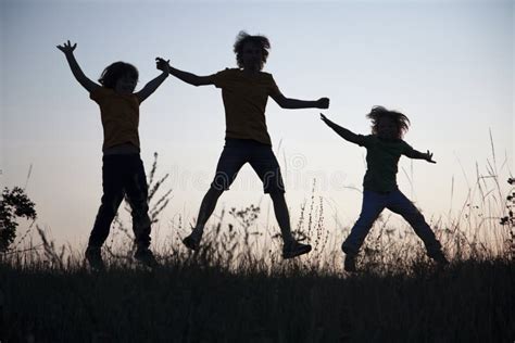Children Playing Jumping On Summer Sunset Meadow Silhouetted Stock