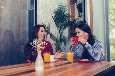 Happy Female Friends Talking And Drinking Coffee While Looking Each In