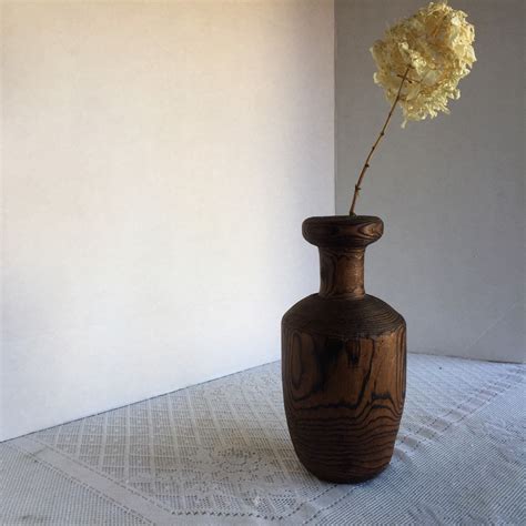 A Wooden Vase With A Yellow Flower In It Sitting On A White Table Cloth