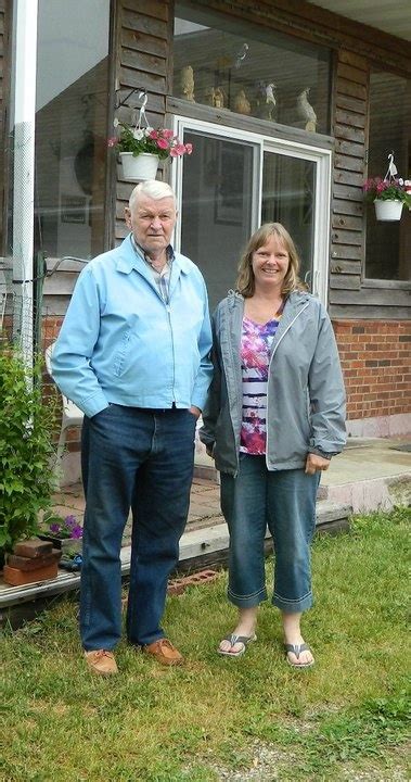 An Older Man And Woman Standing In Front Of A House With Potted Plants
