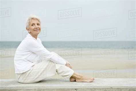 Senior Woman Sitting At The Beach Looking Up And Smiling Stock Photo Dissolve