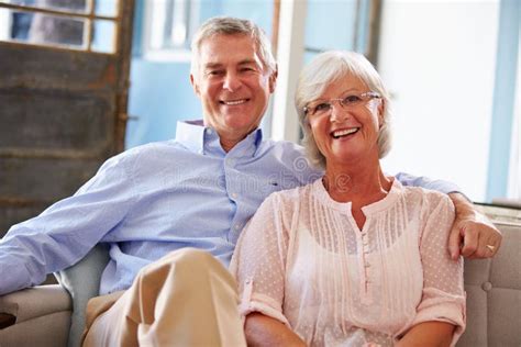 Portrait Of Smiling Senior Couple Sitting On Sofa At Home Stock Image