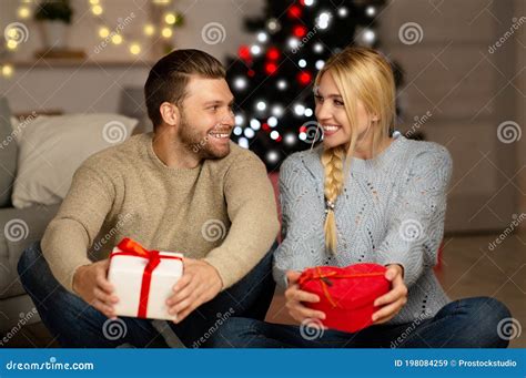 Cheerful Married Couple Holding Christmas Presents Looking At Each
