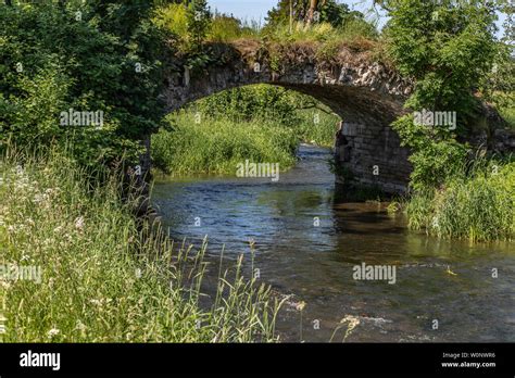 An Old Stone Bridge Overgrown With Grass Crosses The Stream Summer