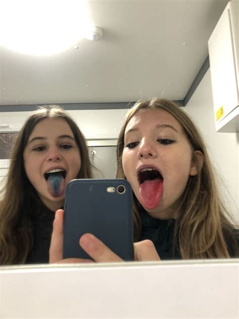 Two Girls Are Taking A Selfie In The Mirror With Their Mouths Open And One Girl Is Sticking Her