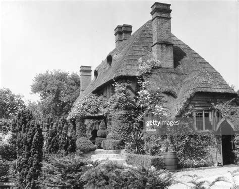 An Archetypal English Country Cottage With Thatched Roof And Rose