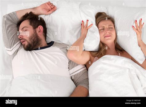 couple in bed man snoring and woman can t sleep covering ears with pillow for snore noise