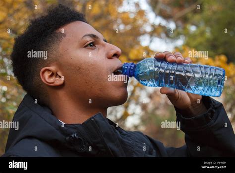 Young Black Man Drinking Water From A Plastic Bottle In The Field On A