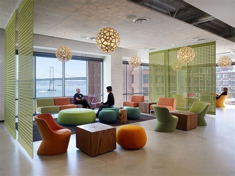 Two People Sitting In An Office Lobby With Colorful Furniture And Large
