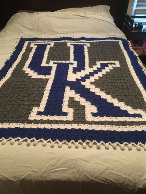 A Crocheted Blanket On Top Of A Bed With White And Blue Trims