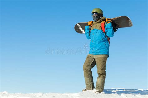 Snowboarder In Helmet Standing At The Top Of A Mountain And Holding His