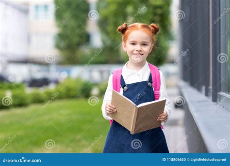 Adorable Cheerful Redhead Schoolgirl Holding Book And Smiling Stock