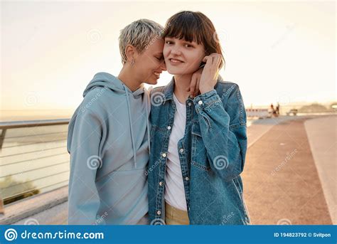 lesbian couple posing at camera standing on the bridge and hugging while watching the sunrise