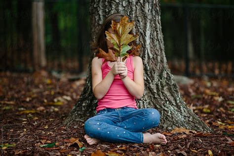 Young Girl Sitting Against A Tree With Leaves In Front Of Her Face By