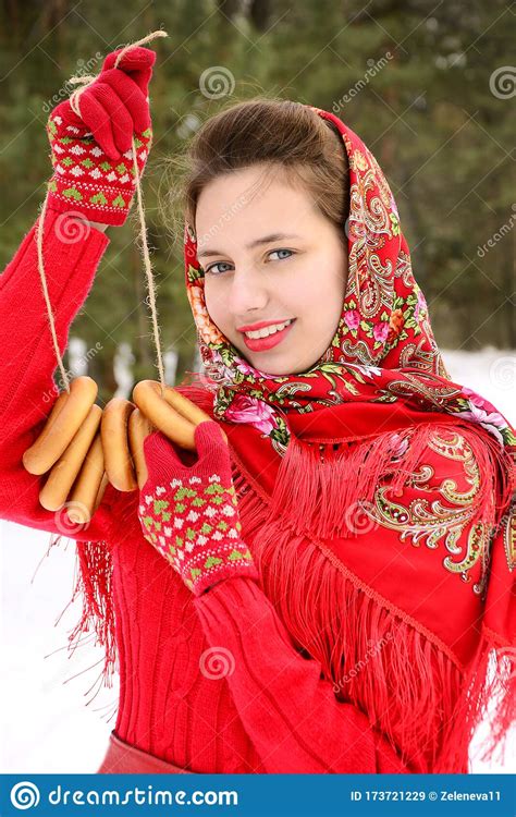 beautiful russian girl in a red traditional shawl holds bagels in the hands of a winter forest