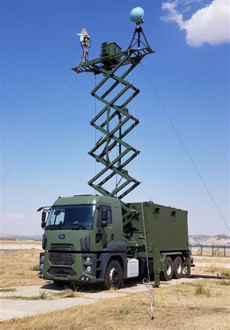 A Man Standing On Top Of A Green Truck Next To A Tall Tower With Ladders