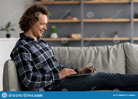 Freelancer Guy Using Laptop Sitting On Couch At Home Side View Stock