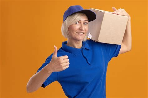 Free Photo Smiling Middle Aged Blonde Delivery Woman In Blue Uniform And Cap Holding Cardbox