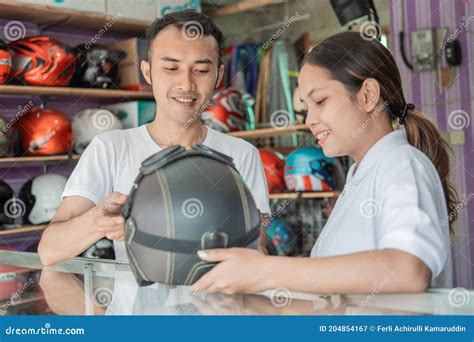 Male And Female Shop Assistants Holding A Helmet Against A Helmet Display Rack Background Stock