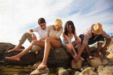 Group Of Friends Sitting Together On Rocks On Beach Looking In Rock Pools Stock Photo Dissolve