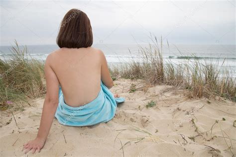Hübsche Frau nackt sitzt von hinten am Strand Stockfotografie