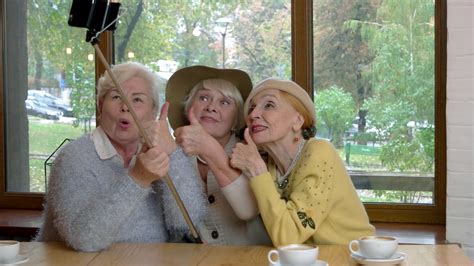 Ladies taking selfie at table. Senior women showing thumbs up ...