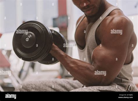 cropped close up of a muscular strong african male athlete lifting heavy dumbbell pumping his