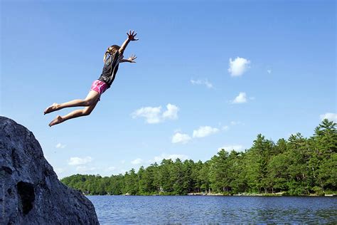 girl jumps off big rock into lake in summer by stocksy contributor cara dolan stocksy