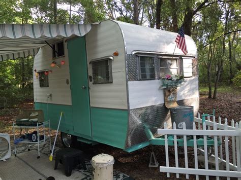 An Old Camper Trailer Is Parked In The Woods Near A White Picket Fence