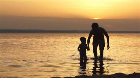 Shirtless Father With Son Walking At Beach During Sunset Stock Photo