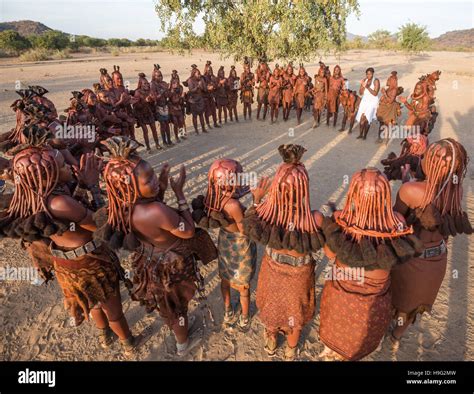 women from himba people in traditional clothes and haircuts are standing in a circle and dancing