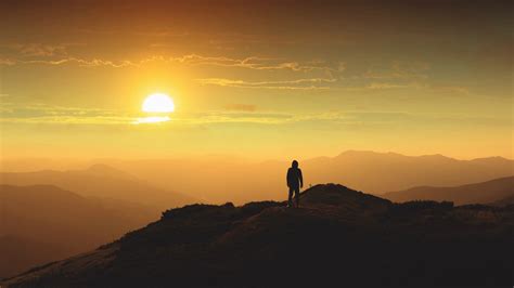 The Man Standing On A Mountain Top Against A Beautiful Sunrise Time