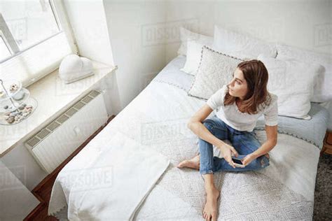 High Level View Of Beautiful Young Woman Sitting On Bed Gazing Through