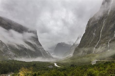 Dark Storm Clouds Cover The Sky Over A Lush Mountain Valley Waterfall