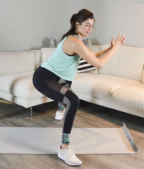 A Woman Is Standing On A Yoga Mat In Front Of A Couch And Stretching