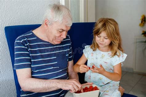 Grandpa And Granddaughter Eating Raspberries At Home Happy Preschool Girl And Senior Man Having