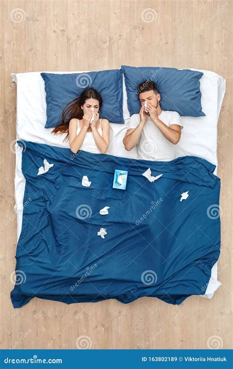Bedtime Young Couple Lying Under Blanket On Bed Top View Blowing Nose