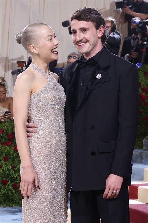 A Man In A Tuxedo Standing Next To A Woman In A Gown On The Red Carpet