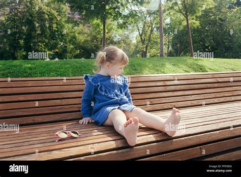 Little Girl Sitting On The Bench In A City Park On A Warm Sunny Day