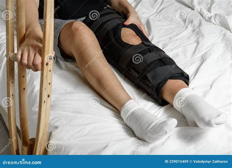 Female Patient Wearing Orthosis Sitting On Bed Holding Crutches After